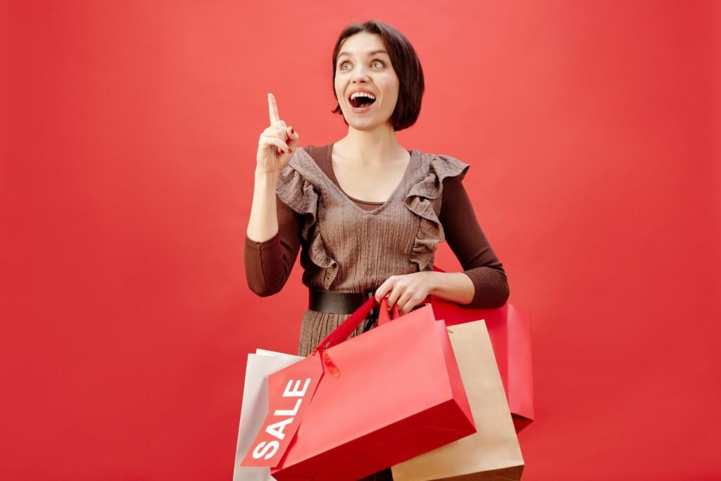 Cheerful woman with shopping bags celebrating a sale on a vibrant red backdrop.